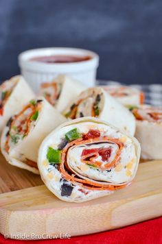 several wraps are stacked on a cutting board with dipping sauce