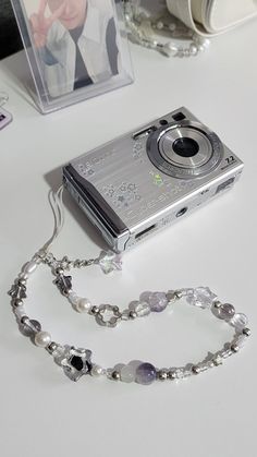 a silver camera sitting on top of a white table next to a necklace and photo frame