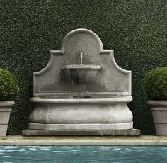 an outdoor fountain surrounded by potted plants next to a pool with water running from it