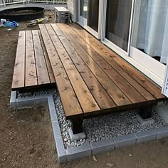 a wooden bench sitting on top of a gravel covered ground next to a building with sliding glass doors