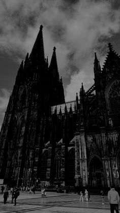 black and white photograph of people walking in front of a large cathedral with tall towers