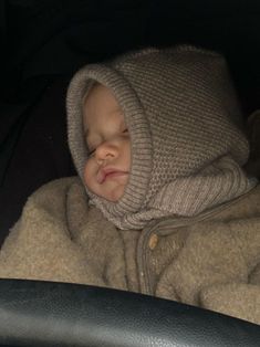 a baby sleeping in a car seat wearing a hood