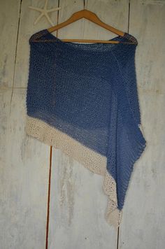 a blue and white knitted shawl hanging on a wooden hanger against a wall