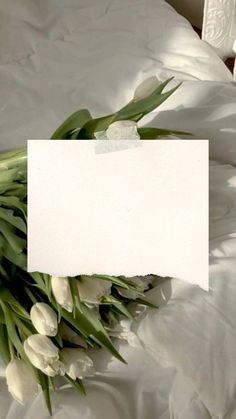 white tulips are on the bed with a note pinned to it's side