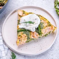 a white plate topped with a piece of quiche covered in cheese and sauce next to asparagus