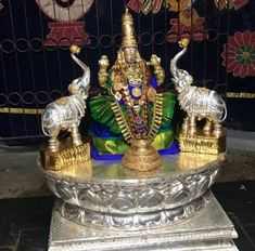 a statue of lord ganeshra sitting on top of a silver stand in front of a wall