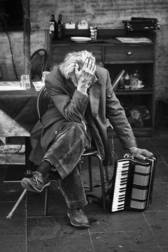 an old man sitting in a chair with his hand on his face while playing the accordion