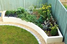 an outdoor garden with various plants and flowers in the center, along side a fence