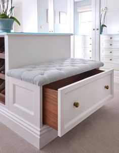 a white bench with drawers underneath it and a potted plant in the corner next to it