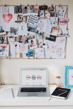 a laptop computer sitting on top of a desk next to a wall covered in pictures