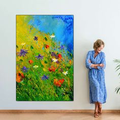 a woman standing in front of a painting on the wall next to a plant and potted plant