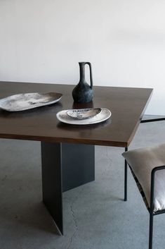 a black vase sitting on top of a wooden table next to a plate and chair