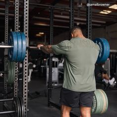 a man is doing squats with barbells in a gym area while another man works on his back