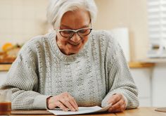 an older woman sitting at a table writing on a piece of paper