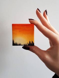 a woman's hand holding up an orange and yellow card with trees on it