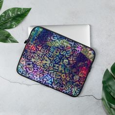 a colorful laptop case sitting on top of a white table next to a green plant