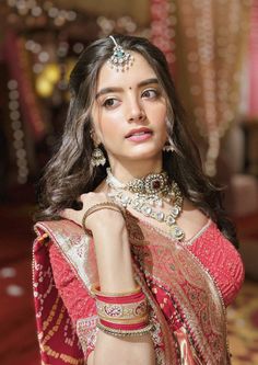 a woman in a red and gold sari with jewelry on her neck, posing for the camera