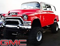 an old red truck parked in front of a white wall with the gmc logo on it