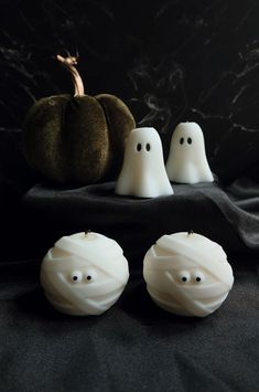 three candles with ghost faces on them sitting next to a black cloth and pumpkins