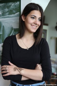 a woman standing with her arms crossed and tattoos on her chest smiling at the camera