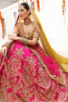 a woman in a pink and gold bridal gown sitting on steps with her arms crossed