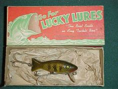 an old fishing lure in its box on a green tableclothed surface, with the label for lucky lures