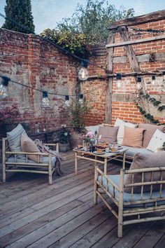 two chairs and a table on a wooden deck with brick walls in the back ground