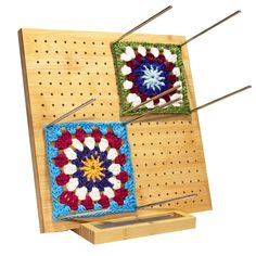 two crocheted squares on a pegboard with knitting needles