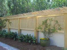 a wooden fence next to a white wall with plants growing on it and some trees in the background