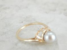 Simple and classic, this pearl ring has a well proportioned gold band, and four balanced prongs set on each side of the pearl. The pearl has a creamy grey luster with pink undertones and makes the perfect understated piece. Metal: 14K Yellow Gold Gem: Grey Pearl Gem Measurements: 6.4 mm, Round Accents: Diamond .04 Carat Ring Size: 4.25 Marks: "14K" Stamped on the inside band Classic Oval Akoya Pearl Ring, Classic Yellow Gold Pearl Ring With Charm, Classic Yellow Gold Ring With Pearl Charm, Classic Yellow Gold Rings With Pearl Charm, Classic Pearl Charm Ring For Wedding, Classic Wedding Rings With Pearl Charm, Pearl Grey, Pearl Ring, Diamond Solitaire