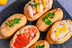 several different types of food in breads on a black plate next to lemon wedges