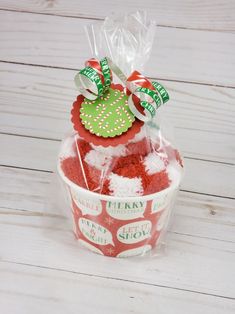 a cupcake in a plastic container on a white wooden table with a green and red bow