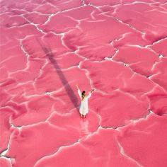 a woman standing in the middle of a pink lake with her arms up to the sky