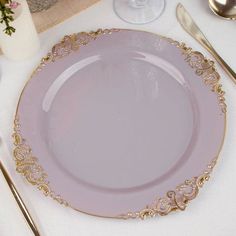 a pink plate with gold trim sits on a white table cloth next to silverware