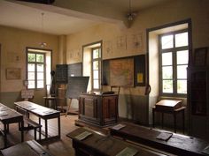 an old school room with desks, chairs and chalkboards on the wall in front of windows