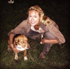 a woman kneeling down next to a brown and white dog on top of a grass covered field