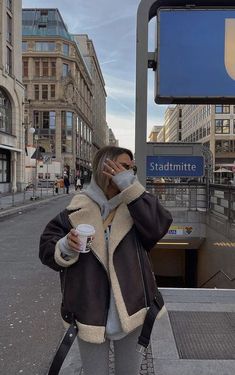 a woman is standing on the sidewalk talking on her cell phone and holding a coffee cup