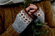 a person wearing a brown and white knitted mitt holding a small green plant