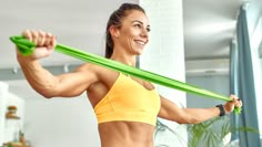 a woman in a yellow sports bra is holding a green tube and smiling at the camera