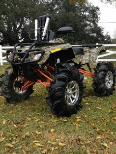 an atv is parked in the grass near a white fence and some leaves on the ground