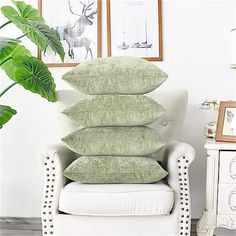 four pillows stacked on top of each other in front of a white chair with a green plant