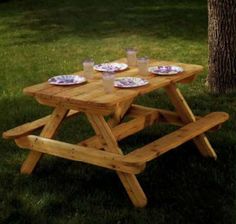 a wooden picnic table with plates and glasses on it in the grass next to a tree