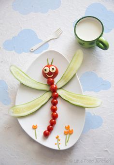 a plate with a dragon made out of vegetables on it and a cup of milk next to it