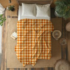 an orange and white checkered blanket on top of a bed next to two pillows