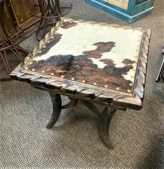 a cow hide ottoman sitting on top of a wooden table in a room filled with chairs