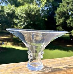 a clear glass vase sitting on top of a wooden table next to some green trees