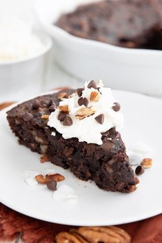 a slice of chocolate cake with whipped cream on top and pecans in the background