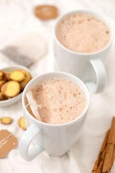 two white mugs filled with hot chocolate and cinnamon sticks on top of a table