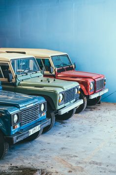 four different colored land rovers parked next to each other in front of a blue wall