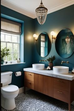 a bathroom with blue walls and two round mirrors above the sinks, along with a white toilet